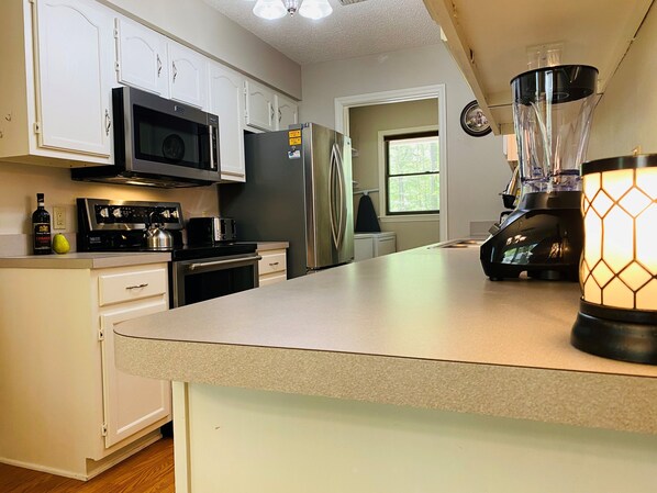A kitchen with white cabinets, a microwave, a refrigerator, a toaster, and a blender.