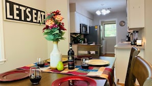 Un coin repas avec une table dressée pour quatre personnes, un vase rempli de fleurs et un panneau sur lequel on peut lire : « À TABLE ! »
