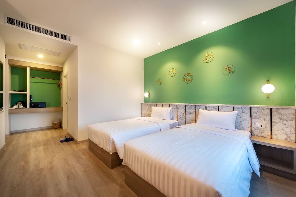 Habitación de hotel con dos camas, una pared de acento verde y un cabecero de mármol.