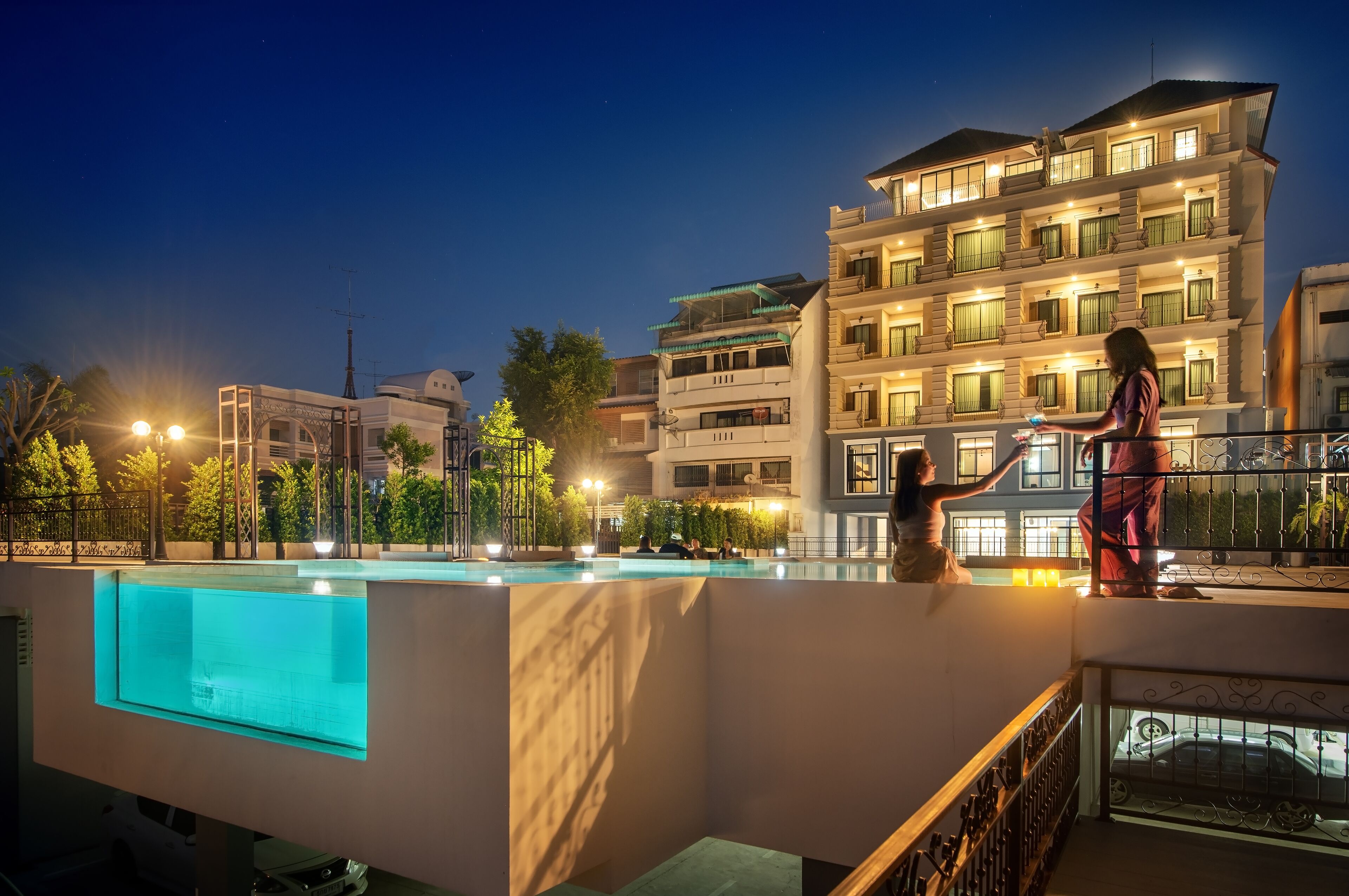 A modern hotel with a swimming pool, outdoor lighting, and a well-maintained garden.