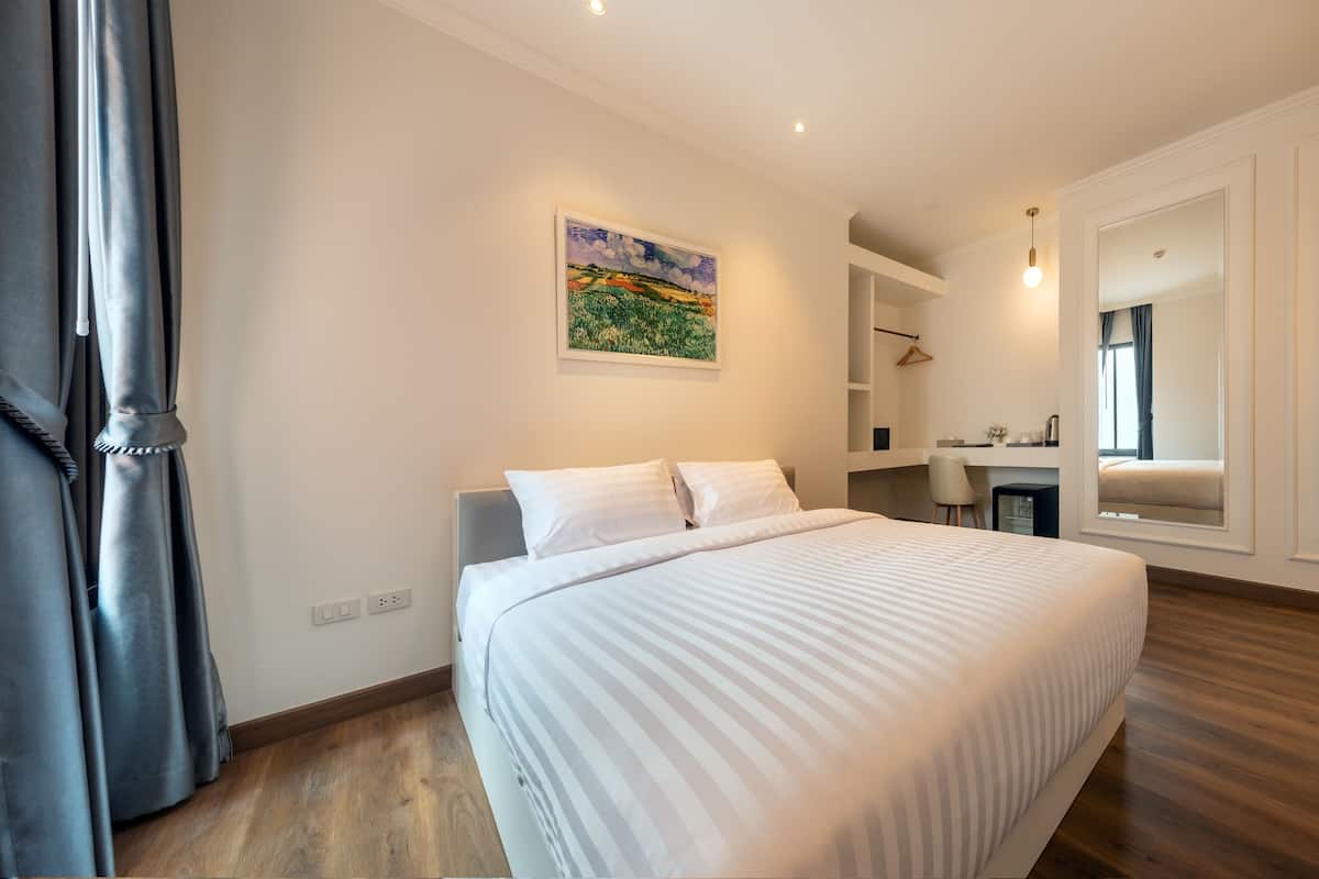 Una habitación de hotel moderna con una cama grande, un cuadro en la pared, un escritorio con una silla y un espejo que refleja la habitación.
