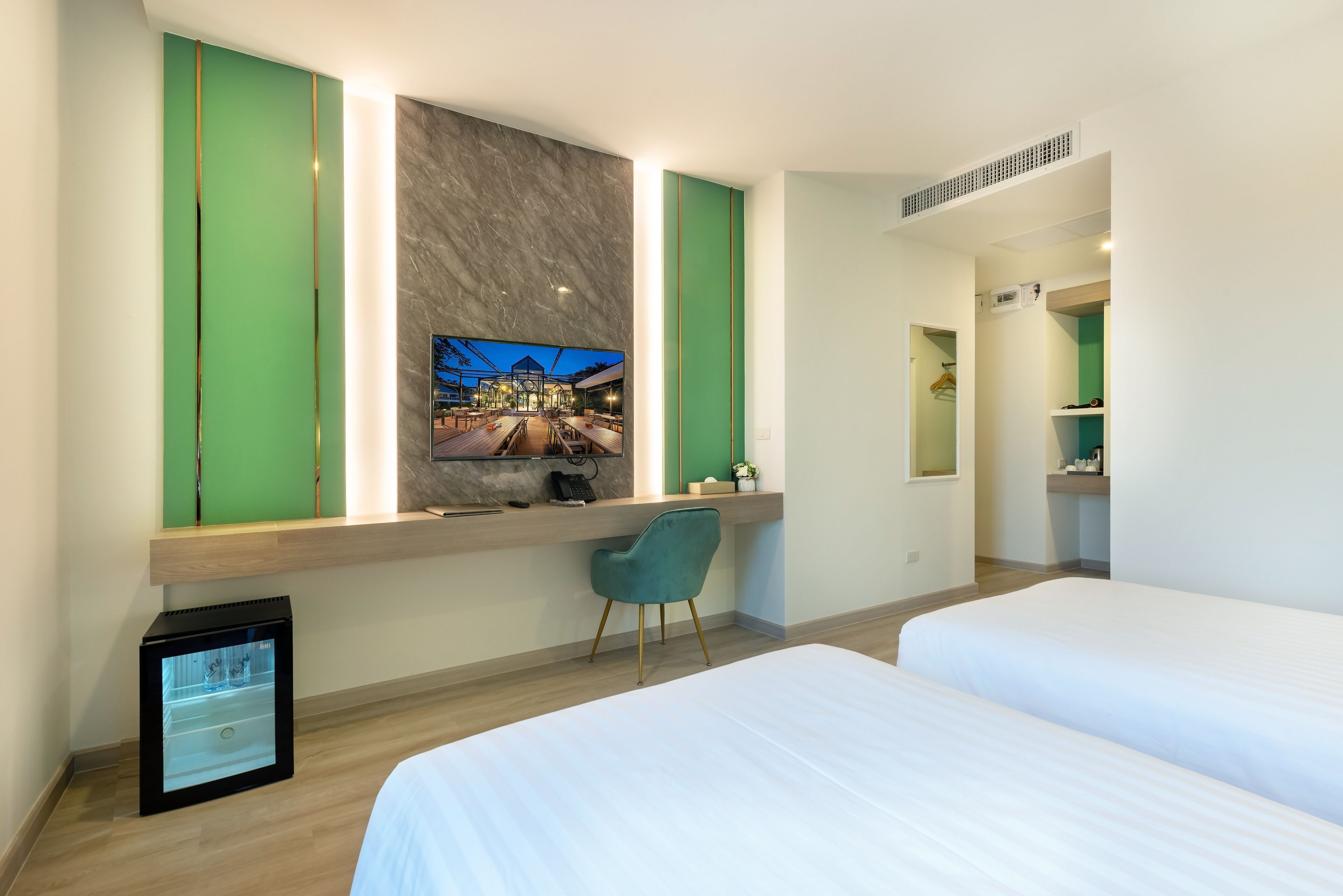 A hotel room with a bed, a desk with a chair, a TV mounted on the wall, and a small refrigerator.
