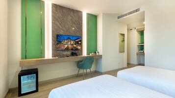 A hotel room with a bed, a desk with a chair, a TV mounted on the wall, and a small refrigerator.