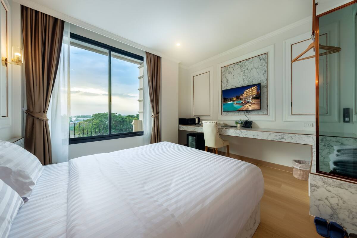 Habitación de hotel con una cama grande, un escritorio, un televisor y vistas al exterior.