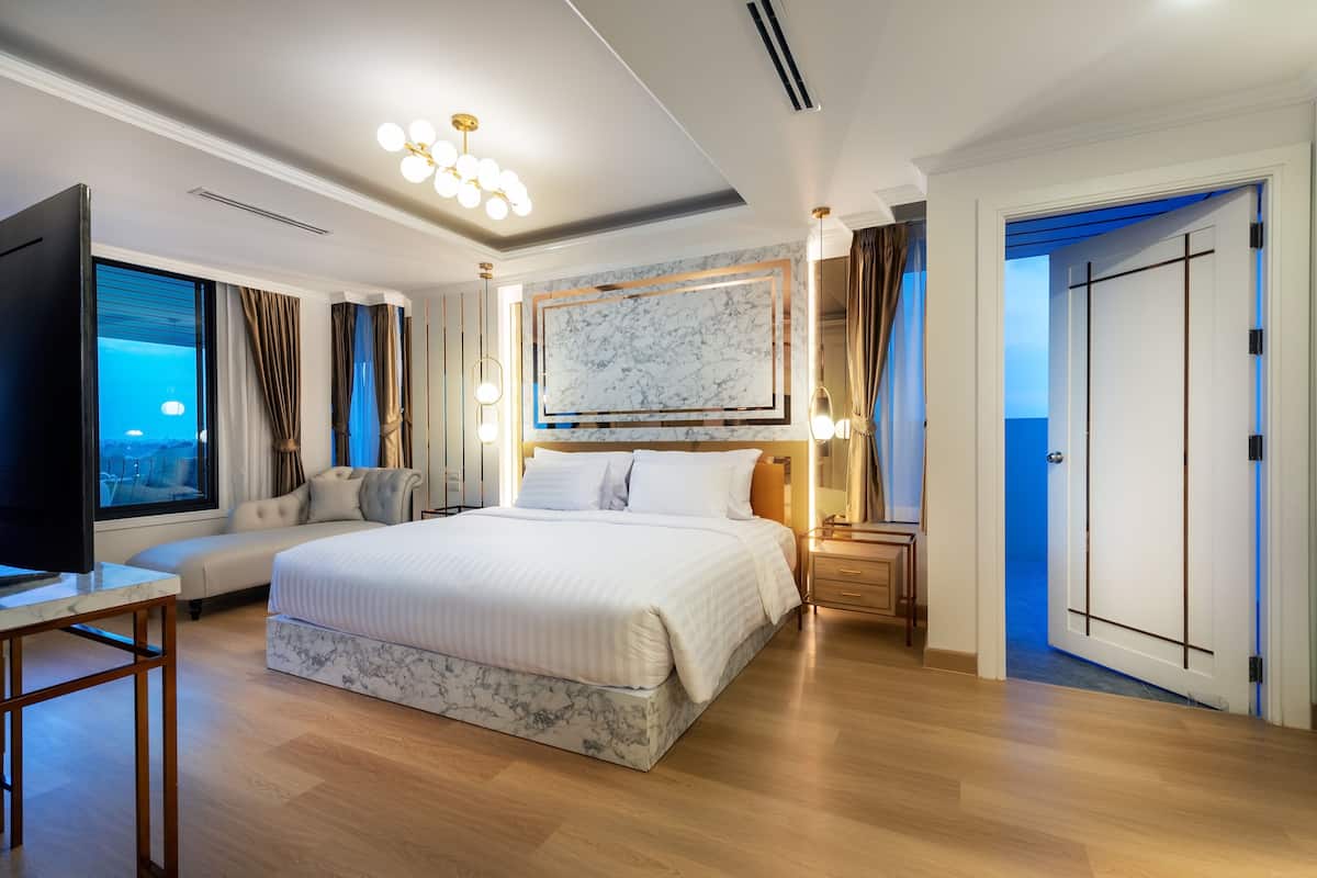 Un dormitorio amplio con una cama grande, un televisor, un cabecero con diseño de mármol y vistas al océano a través de la ventana.