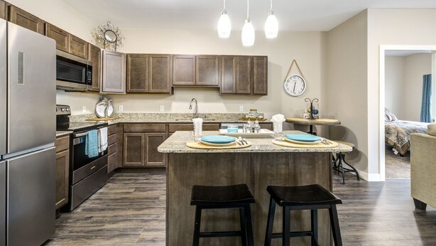 Cocina moderna con encimeras de granito, electrodomésticos de acero inoxidable, armarios de madera y una isla central con taburetes.