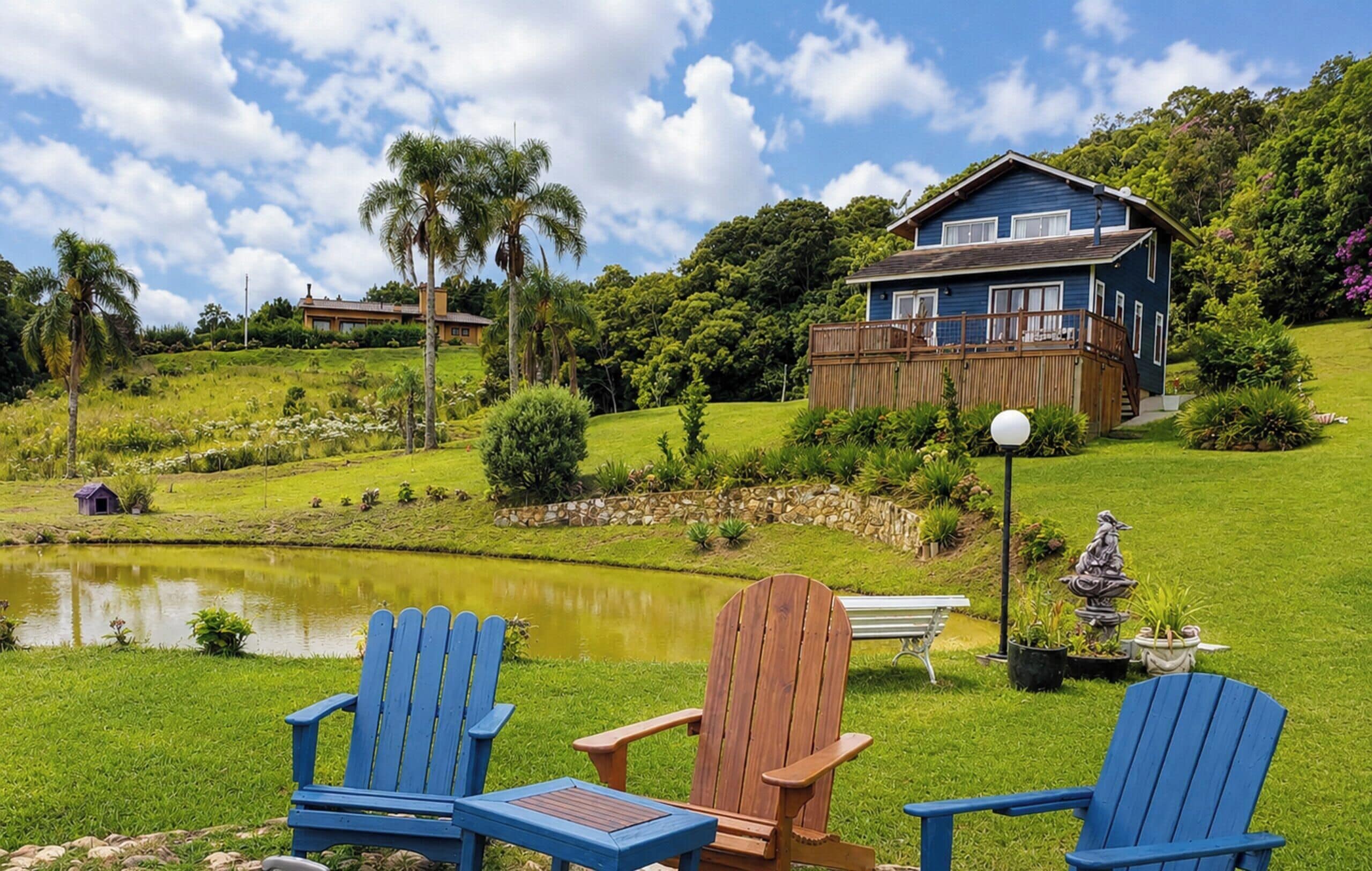 A house with a pond, a wooden deck, and two blue Adirondack chairs.