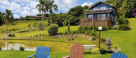 A house with a pond, a wooden deck, and two blue Adirondack chairs.