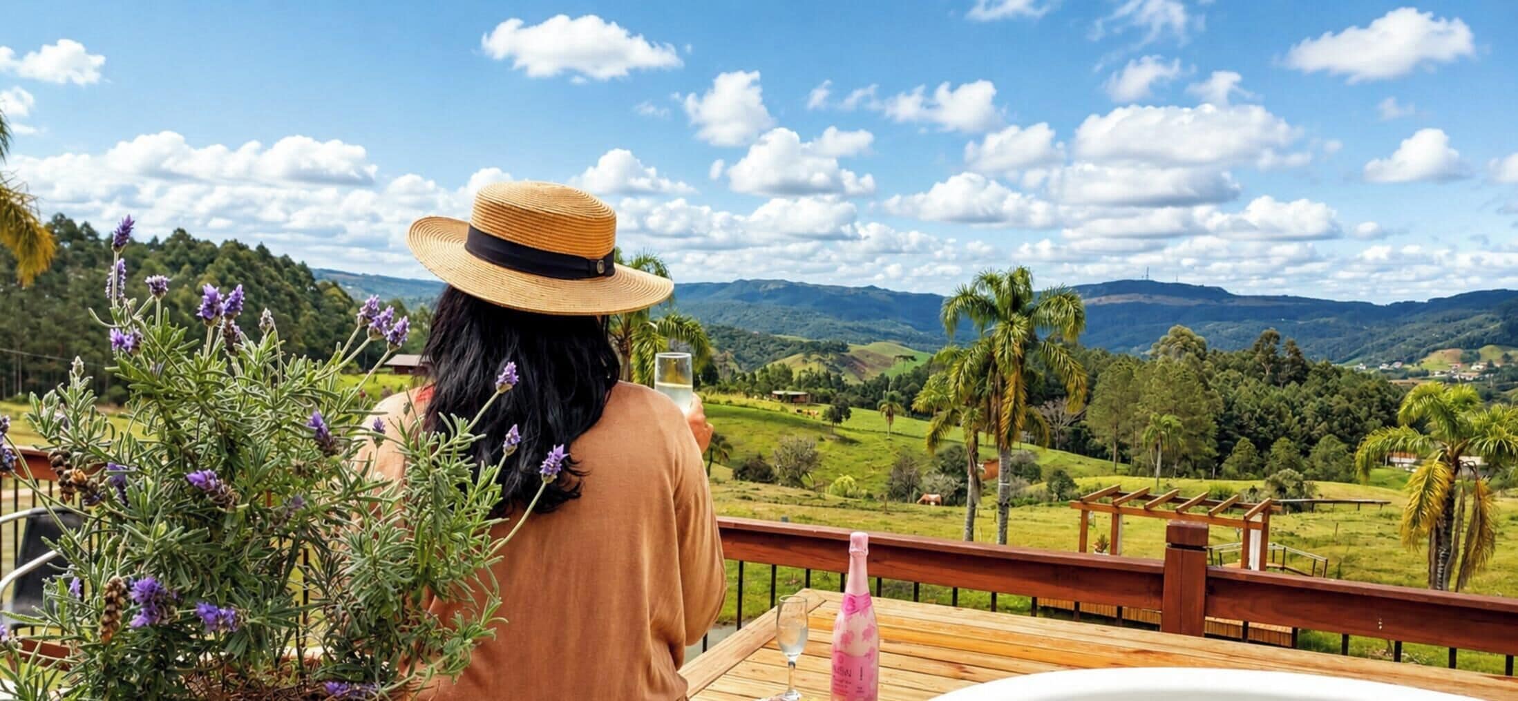 A person with a straw hat overlooking a scenic landscape from a wooden deck.