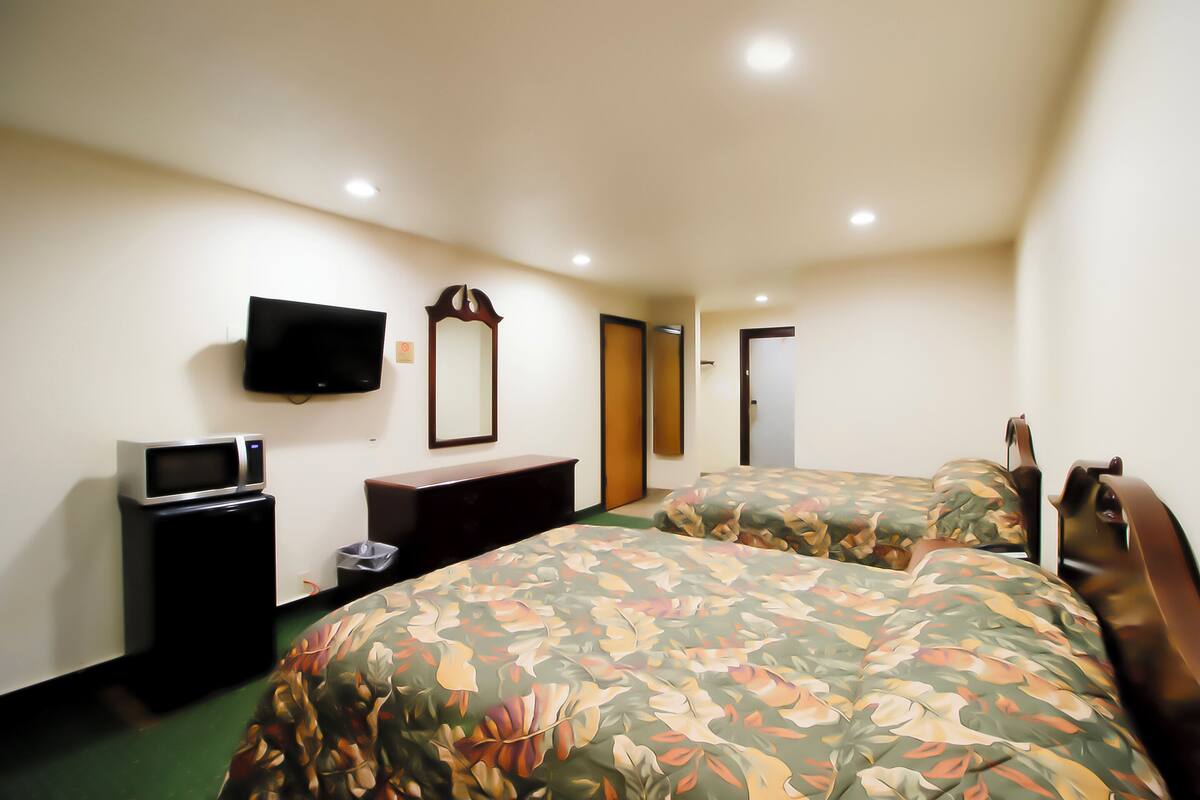 A hotel room with two beds, a flat-screen TV, a microwave, a trash bin, and a mirror.
