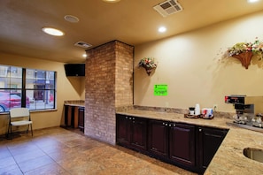 A kitchen area with a brick column, a coffee machine, and a sign indicating '1 PER PERSON PLEASE BE CONSIDERATE OF OTHERS'. - OYO Pinewood Inn & Suites Silsbee GA (Silsbee)