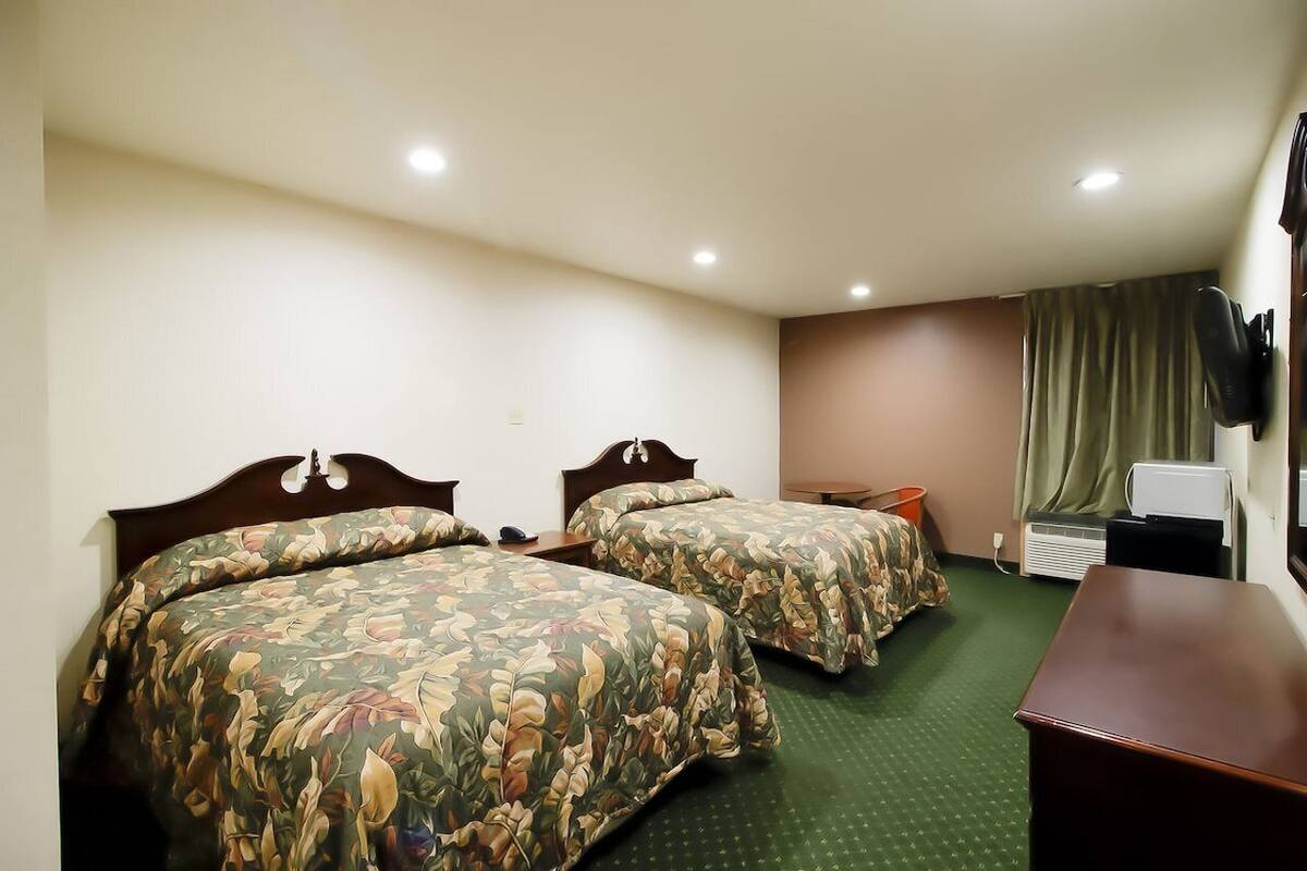 A hotel room with two single beds, a desk, a chair, a TV, and a window with curtains.
