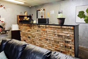 A reception area with a brick wall, a black counter, and a couch. - OYO Pinewood Inn & Suites Silsbee GA (Silsbee)