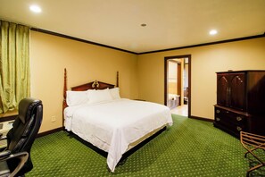 A hotel room with a large bed, a wooden headboard, a green patterned carpet, a wooden wardrobe, and a chair. - OYO Pinewood Inn & Suites Silsbee GA (Silsbee)