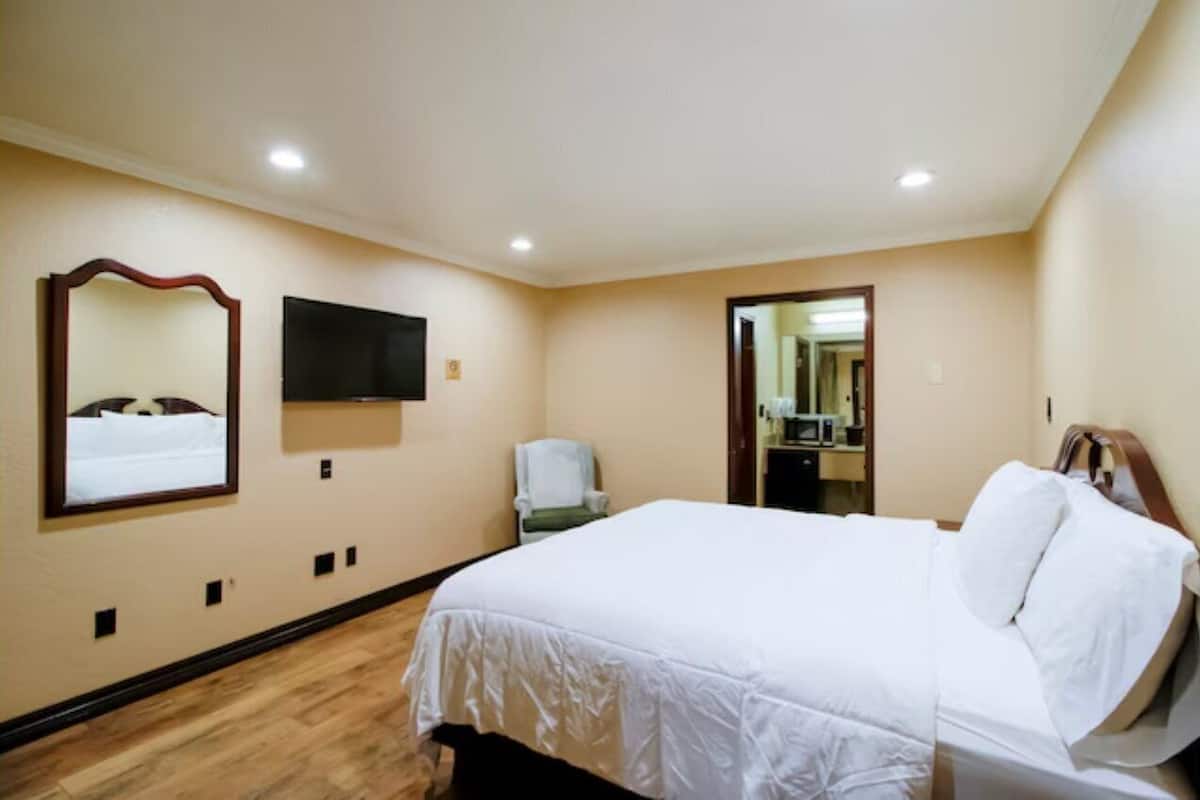 A hotel room with a large bed, a flat-screen TV mounted on the wall, a chair, and a door leading to a bathroom.