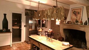 A kitchen with a wooden island, a stainless steel refrigerator, a fireplace, and a hanging light fixture. - LE MAS DES COSME EN PROVENCE (Aramon)