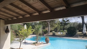 A covered outdoor area with a pool, potted plants, and outdoor furniture. - LE MAS DES COSME EN PROVENCE (Aramon)