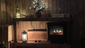 L’intérieur d’un chalet chaleureux, avec un mur en bois, un sapin de Noël illuminé, une cheminée et une pancarte indiquant « Chalet de Houghton Lake ».