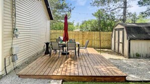Une terrasse en bois avec une table et des chaises, un parasol rouge et un abri de jardin dans un jardin.
