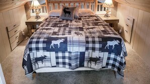 Une chambre mansardée chaleureuse, avec un couvre-lit à carreaux orné de motifs animaliers, des murs en bois et un plafond en pente.