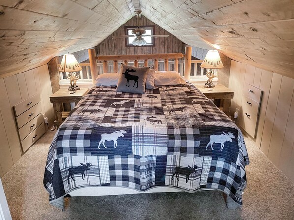 Ein gemütliches Schlafzimmer im Dachgeschoss mit karierter Bettdecke und Tiermotiven, Holzwänden und einer geneigten Decke.