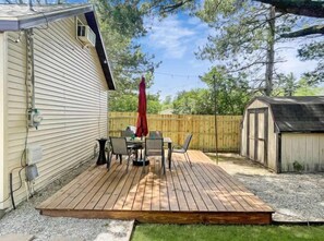 Eine Holzterrasse mit Tisch und Stühlen, einem roten Sonnenschirm und einem Gartenhaus im Hinterhof.