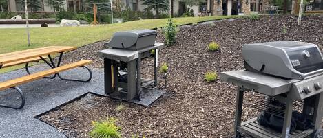 An outdoor patio area with a barbecue grill, picnic table, and umbrellas.