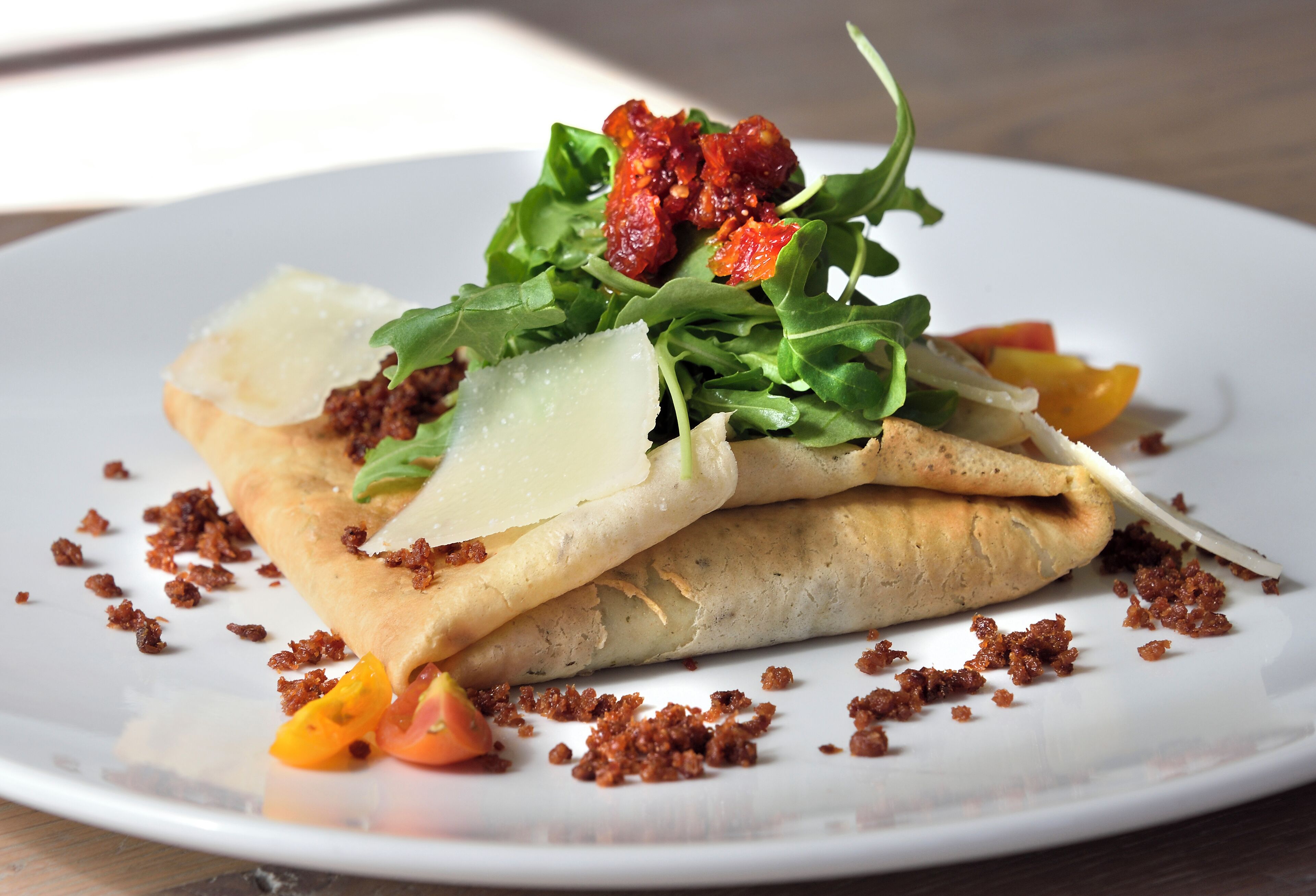 A plate with a rolled dish, garnished with greens, cheese, and tomato slices.