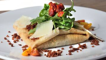 A plate with a rolled dish, garnished with greens, cheese, and tomato slices.