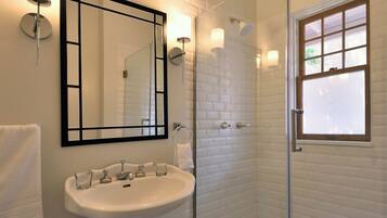 A bathroom with a pedestal sink, a large mirror, and a glass-enclosed shower.