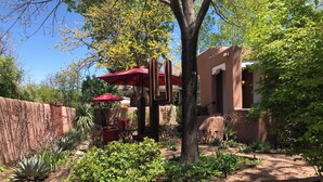 Un patio con sombrilla roja, un cactus y un muro de ladrillo.