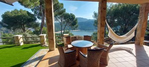 Un patio con mobiliario de mimbre y una hamaca con vistas a un lago y montañas.