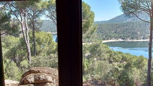 Vista de dentro de um edifício, com vista para um lago rodeado por árvores e montanhas.
