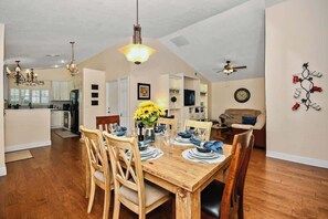 A dining area with a wooden table set for four, surrounded by wooden chairs. A chandelier hangs from the ceiling, and a ceiling fan is visible. - Beautiful 4/2, Golf, Pool & Games! (Sanford)