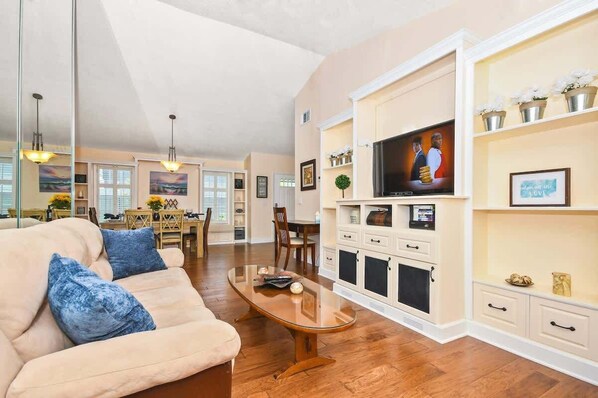 A spacious living room with a beige sofa, a wooden coffee table, and a TV on a white cabinet. - Beautiful 4/2, Golf, Pool & Games! (Sanford)
