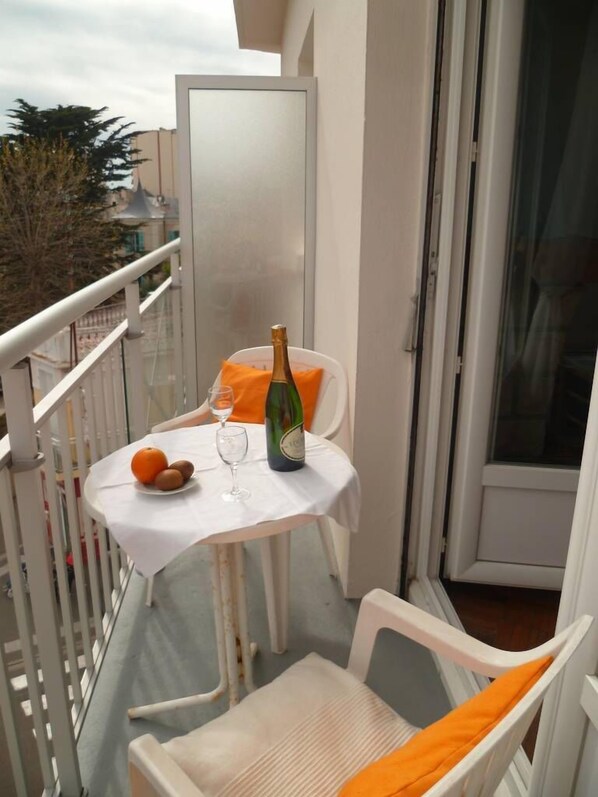 A balcony with a table set for two, a bottle of champagne, and a chair with an orange cushion.