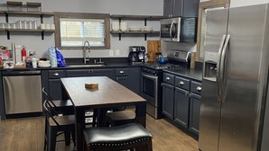 A modern kitchen with dark wood cabinets, stainless steel appliances, and a wooden dining table with stools.