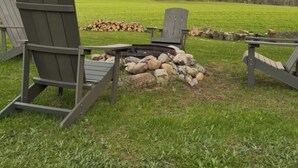 A fire pit with chairs and logs in a grassy field.