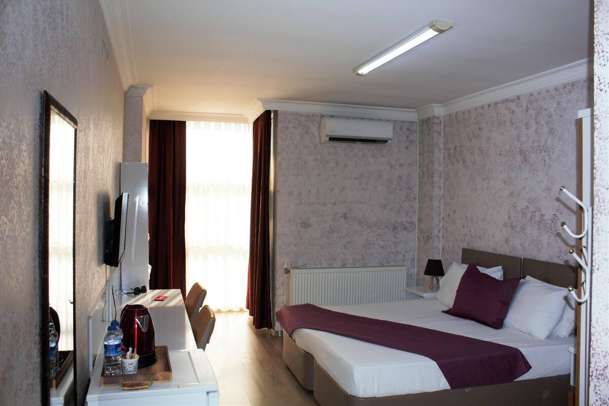A hotel room with a bed, a desk with a chair, a television, and a window with curtains.