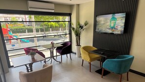Um interior moderno com uma TV fixada na parede, uma janela grande com vista para um parquinho e vários cadeiras e mesas.