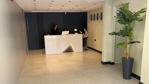 Uma área de recepção com balcão de mármore, planta em vaso e relógios de parede.