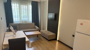Uma sala moderna com sofá, mesa de centro, mesa de jantar com cadeiras, televisão de tela plana na parede e geladeira.