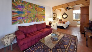 A living room with a red sofa, a glass coffee table, and a colorful abstract painting on the wall.