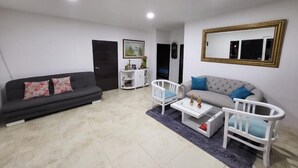 Un salon avec un canapé, un fauteuil blanc, une table basse et un berceau.