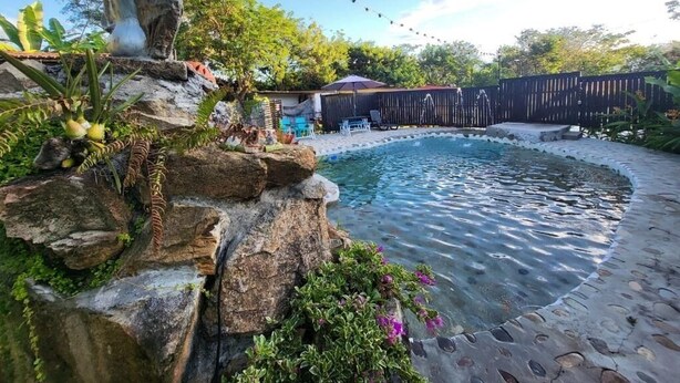 Un jardin avec une piscine, entouré d’une clôture en bois, et une statue posée sur un rocher.