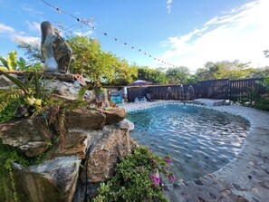 Ein Garten mit Schwimmbad, umgeben von einem Holenzaun, und einer Statue auf einem Felsen.