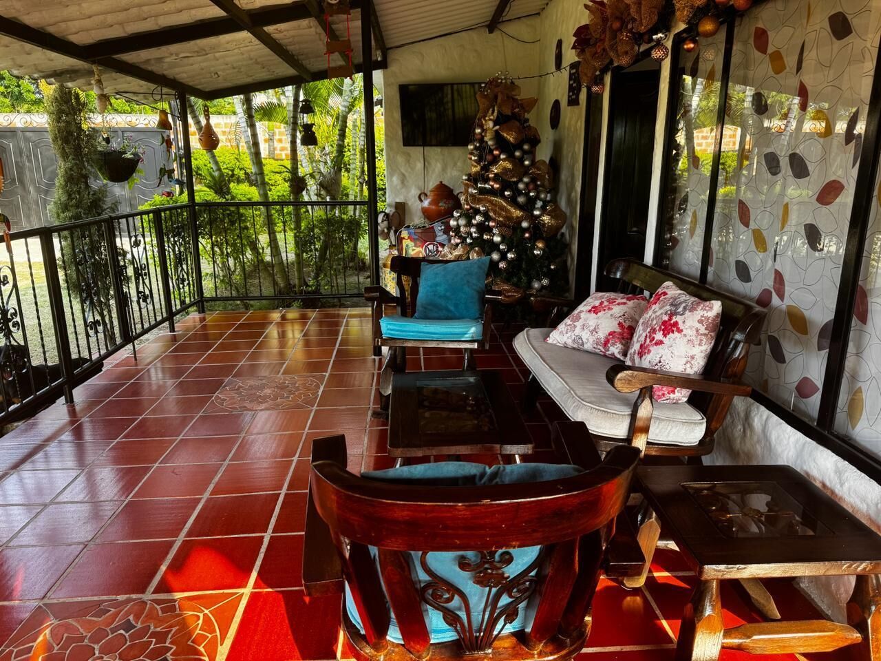 A covered patio with a tiled floor, a wooden chair, a sofa, and a Christmas tree.