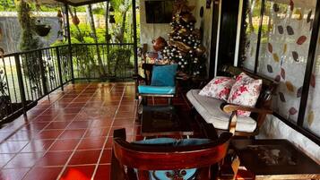 A covered patio with a tiled floor, a wooden chair, a sofa, and a Christmas tree.