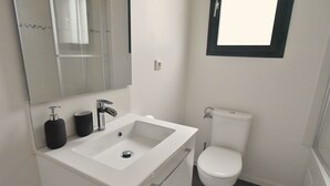 A modern bathroom with a white sink, a mirror, a toilet, and a window. - Cosy, fully-equipped, refurbished F2 (Vert-le-Grand)