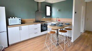 A modern kitchen with white cabinets, a wooden countertop, a microwave, a stove, and a sink. There are four stools around the kitchen island. - Cosy, fully-equipped, refurbished F2 (Vert-le-Grand)